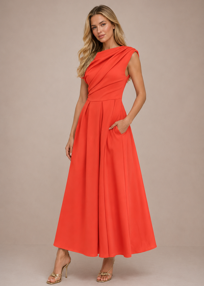 A woman modeling a bright coral-orange sleeveless maxi dress with draped detailing and side pockets, standing against a solid beige studio background.